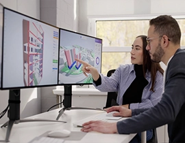 Dos personas frente dos pantallas de ordenador grandes, trabajando juntos