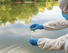 Persona vestida con EPI de laboratorio recogiendo una muestra agua en un río