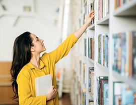Chica joven frente a estantería buscando un libro en una biblioteca 